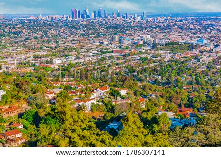 A hilltop view of the urban sprawl of Los Angeles show skyscrapers in the distance and homes built on hillsides in the foreground.
