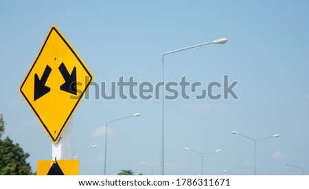 Yellow traffic signs with two white arrow heads indicate the intersection on the road, on blue sky as the background, indicates the concept of making decide of choice to choose the path of life.