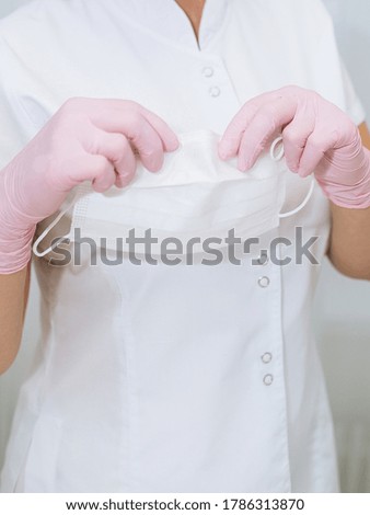 Hand in a pink latex medical gloves. White medical medical mask in hands. Preparation for work in the master's office