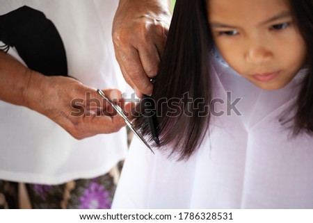 Cute asian child girl getting haircut by grandmother at home
