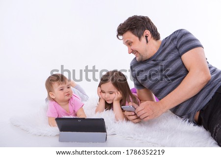 modern technologies in everyday life: a man talks on the phone through a headset, children watch a cartoon on a tablet. Hobbies and recreation with gadgets. Parent with girls on the floor
