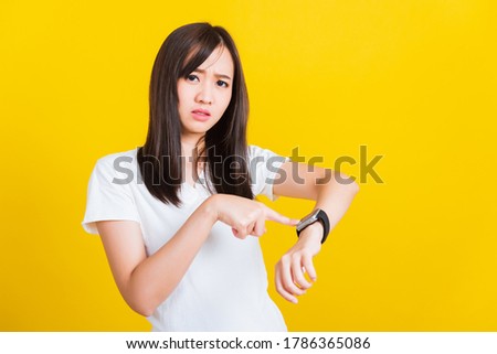 You are late not on time, Portrait Asian of a happy beautiful young woman scared casual girl showing and pointing finger her wristwatch studio shot isolated on yellow background Royalty-Free Stock Photo #1786365086