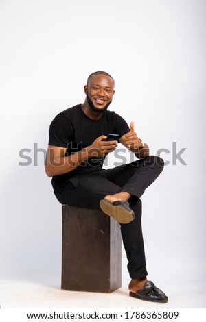 young black handsome man sitting, using his smartphone with happiness