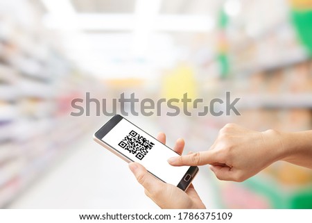 Shopping and Retail Concept  Hand holding smartphone that showing quick response code on white screen and blurry image of supermarket in background.
