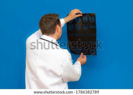 thoughtful caucasian neurological doctor looking at a brain ct scan on blue background. Braing imagining examined by young doctor.