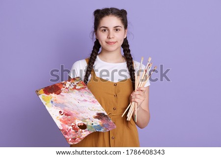 Talented woman creating beautiful watercolor floral design, standing isolated over lilac background, looking directly at camera, wearing casual attire.