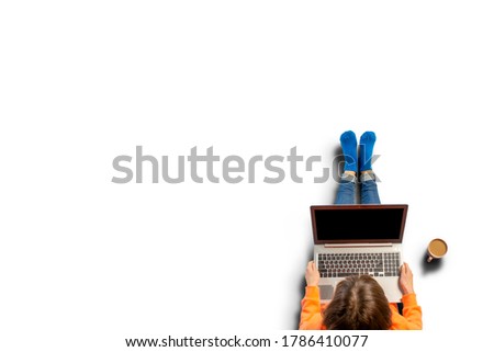 Young woman holding a laptop on his knees, standing next to a cup of coffee. Top view, flat lay