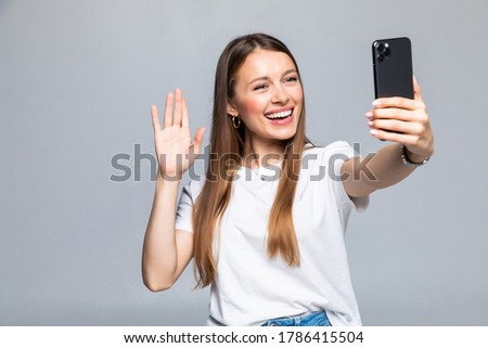 Happy young woman blogger influencer holding modern smart phone wave hand hello. Smiling vlogger girl looking at mobile make video call, shooting vlog taking selfie on grey background Royalty-Free Stock Photo #1786415504
