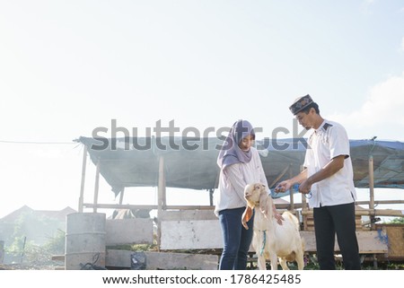 happy muslim couple buy a goat for eid adha sacrifice or qurban celebration Royalty-Free Stock Photo #1786425485