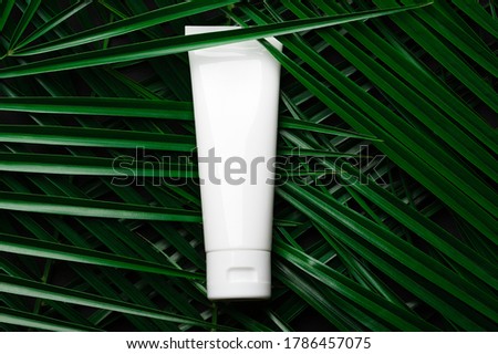 White plastic tube with hand, face, body cream on palm leaves, tropical backdrop. Beauty skin care product template. Dark background, concept of natural care, eco cosmetics. Royalty-Free Stock Photo #1786457075