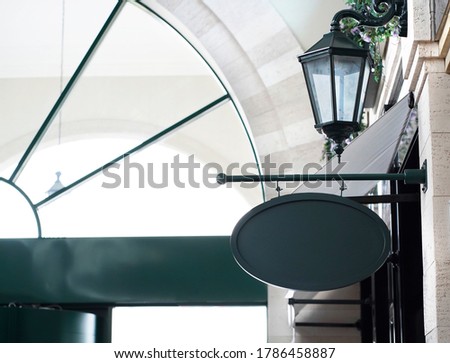 Blurred background of black iron oval street shop mockup template signboard on wall with street lantern.                           