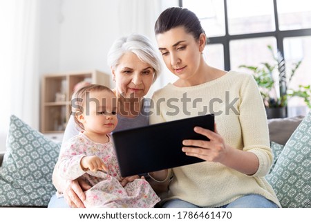 family, generation and technology concept - mother, daughter and grandmother sitting with tablet pc computer on sofa at home