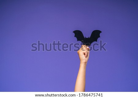 child's hand holds a black paper bat on a purple background. The Concept Of Halloween. Paper cutting style. Front view.