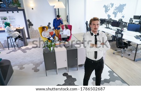 portrait of successful businessman entrepreneur with headphones around his neck and colleagues in the background at busy startup office