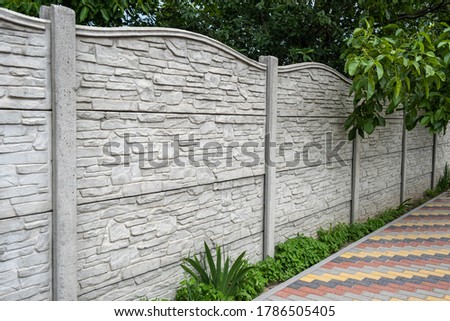 Decorative concrete fence on the background of green trees. Royalty-Free Stock Photo #1786505405