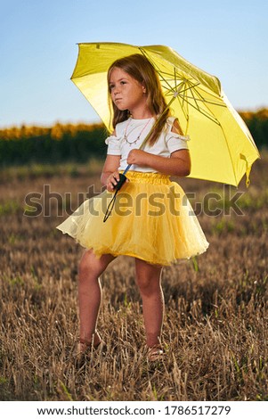 Happy young girl with umbrella on a field with sunflowers in background