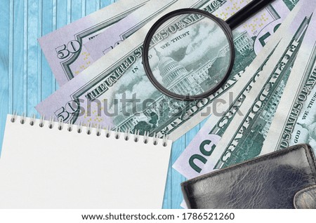 50 US dollars bills and magnifying glass with black purse and notepad. Concept of counterfeit money. Search for differences in details on money bills to detect fake