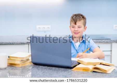 A boy with a blue shirt is engaged remotely on a laptop with a teacher. Smiling while looking at a computer screen. Online Learning Concept