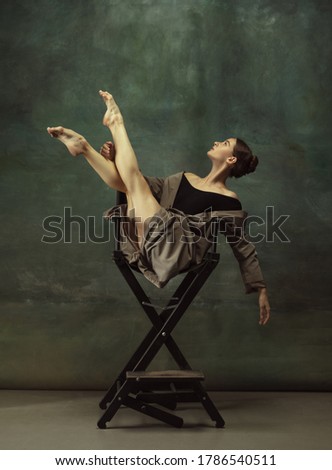 Beautiful portrait, dreamful. Graceful classic ballerina dancing, posing isolated on dark studio background. Stylish trench coat. Grace, movement, action and motion concept. Looks weightless, flexible
