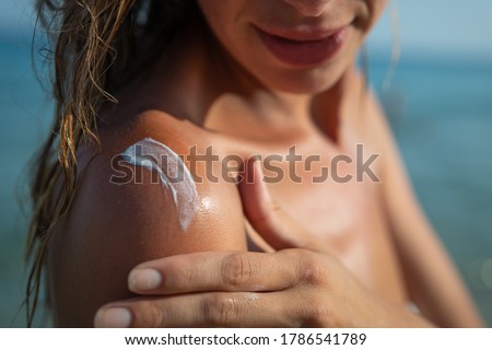 Close up of smiling young woman is applying a sunscreen or sun tanning lotion on a shoulder to take care of her skin on a seaside beach during holidays vacation. Royalty-Free Stock Photo #1786541789