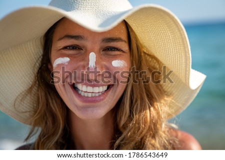 Close up of happy young smiling woman with straw hat and sunscreen or sun tanning lotion on her face to take care and protect skin on a seaside beach during holidays vacation. Royalty-Free Stock Photo #1786543649