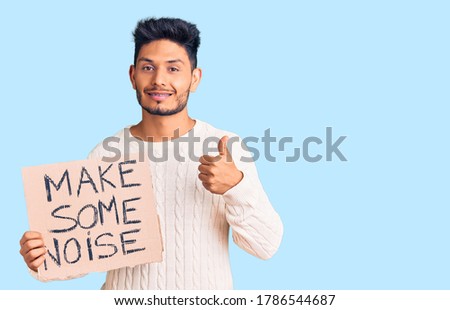 Handsome latin american young man holding make some noise banner smiling happy and positive, thumb up doing excellent and approval sign 