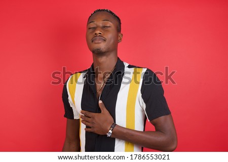African american man with braids wearing casual shirt over isolated red background touches tummy, smiles gently, eating and satisfaction concept.