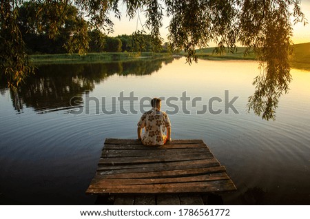 a man sits with his back and looks at the lake