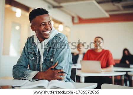 Male student sitting in university classroom looking away and smiling. Man sitting in lecture in high school classroom. Royalty-Free Stock Photo #1786572065