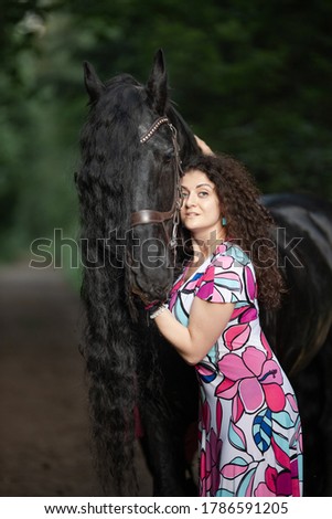 Young brunette woman in a bright dress posing with a frieze horse in a green forest.