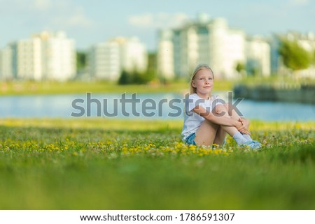 Blonde girl dancing, jumping, doing acrobatics and posing, in a city park on green grass near a lake on a sunny day