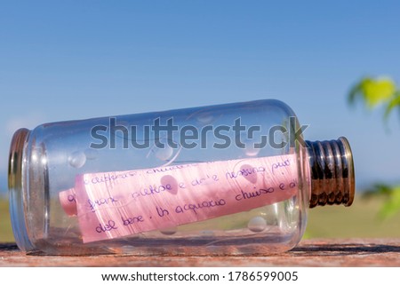 A handwritten letter on a pink sheet is rolled up inside a glass bottle 