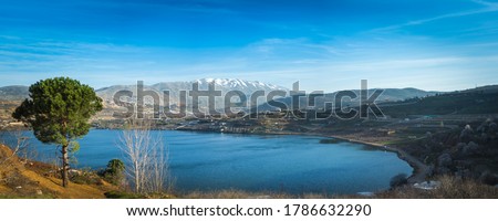 Beautiful panoramic view of Lake Ram (Birkat Ram) - a crater lake (maar) in the northeastern Golan Heights, with a Druze town of Majdal Shams and a snow-capped Mount Hermon in the background Royalty-Free Stock Photo #1786632290
