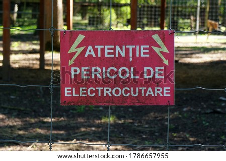 Red sign on wire fence. The Romanian text translates to "Warning. Risk of electric shock". 