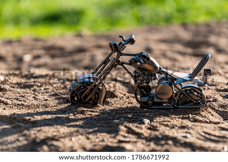 Homemade metal toy model of a road sports motorcycle stands on a sandy road on a green abstract background