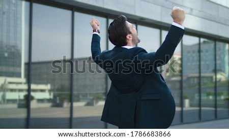 Close up happy businessman celebrating victory near modern building. Young business man getting promotion outdoors. Cheerful man enjoying achievement at urban street. Royalty-Free Stock Photo #1786683866