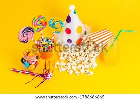 a top view popcorns and lollipops along with cocktail funny cap on the yellow background birthday party drink