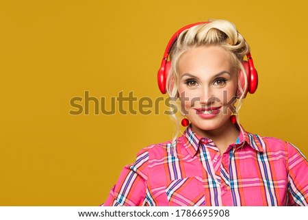 Pretty pinup girl listening music with headphones on bright yellow background. Pretty retro model woman with red lips makeup and vintage fashion hairstyle