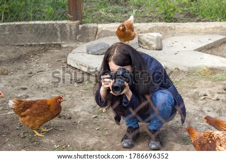 Young girl photographs hens birds in an aviary. Woman hold and looking in camera and takes pictures at farm