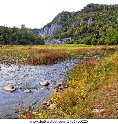Ural. Water autumn landscape. A shallow fast mountain river with a rocky bottom. In the background there are rocks overgrown with forest.