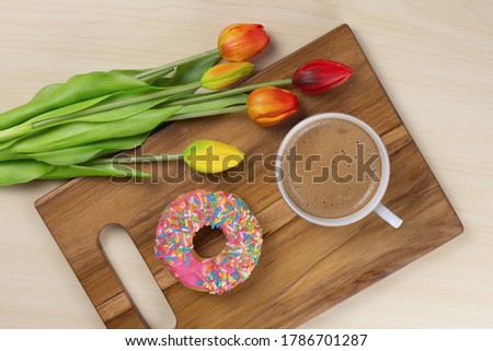 Flat-lay picture a cup of tasty cappuccino and donut on a wooden cutting board.