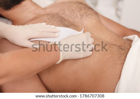 Cosmetologist doing waxing on torso of unrecognizable male client Royalty-Free Stock Photo #1786707308