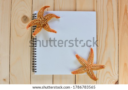 Flat lay notebook with blank and dried starfish on wooden table  for summer holiday concepts. Top view book with copy space. 
