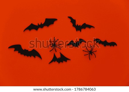 Halloween background, decorations and scary concept. Spiders and black bats fly over orange background. Top view