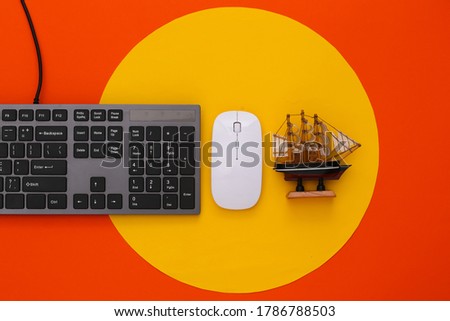 Travel flat lay PC keyboard and ship on orange background with yellow circle. Top view