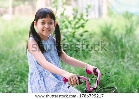 Asian little girl riding her bicycle outside with smile and happy