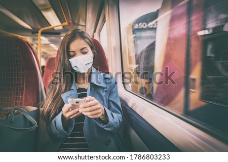Face mask concept. Woman wearing mandatory mask inside public spaces for transport such as train station and bus. Asian woman passenger using mobile phone with face covering on commute. Royalty-Free Stock Photo #1786803233