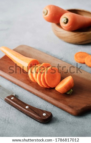 Selected focus of cut pieces carrot on cutting board with knife and fresh carrots at behind. Grain background. Isolated on grey.
