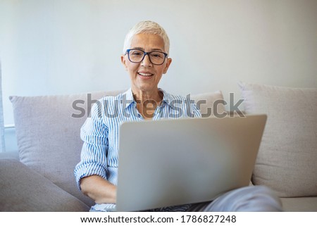 Focused old woman with white hair at home using laptop. Senior stylish entrepreneur wearing eyeglasses working on computer at home. SWoman analyzing and managing domestic bills and home finance. Royalty-Free Stock Photo #1786827248