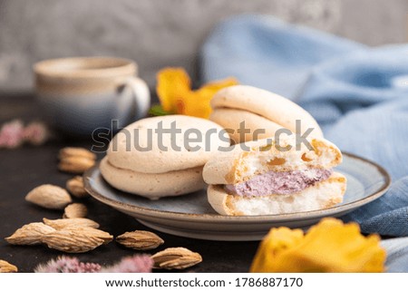 Meringues cakes with cup of coffee on a black concrete background and blue linen textile. Side view, close up, selective focus.